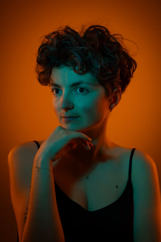 Portrait artistique féminin sur fond orange avec éclairage gélatine cyan, jeune femme aux cheveux bouclés courts