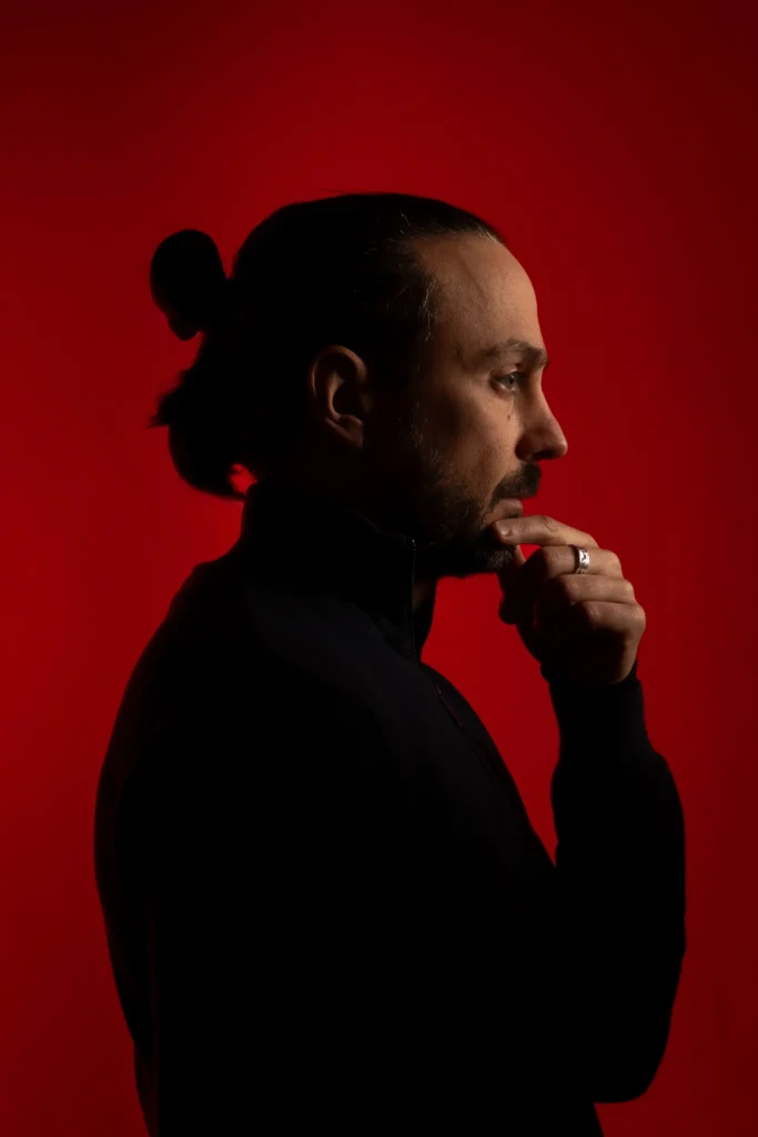 Portrait artistique de David Edighoffer, photographe à Chambéry, de profil sur fond rouge en studio